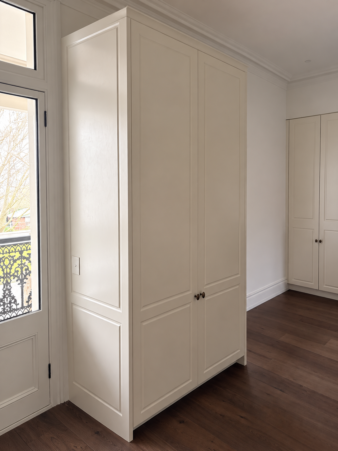 Traditional white panelled cabinetry beside a window