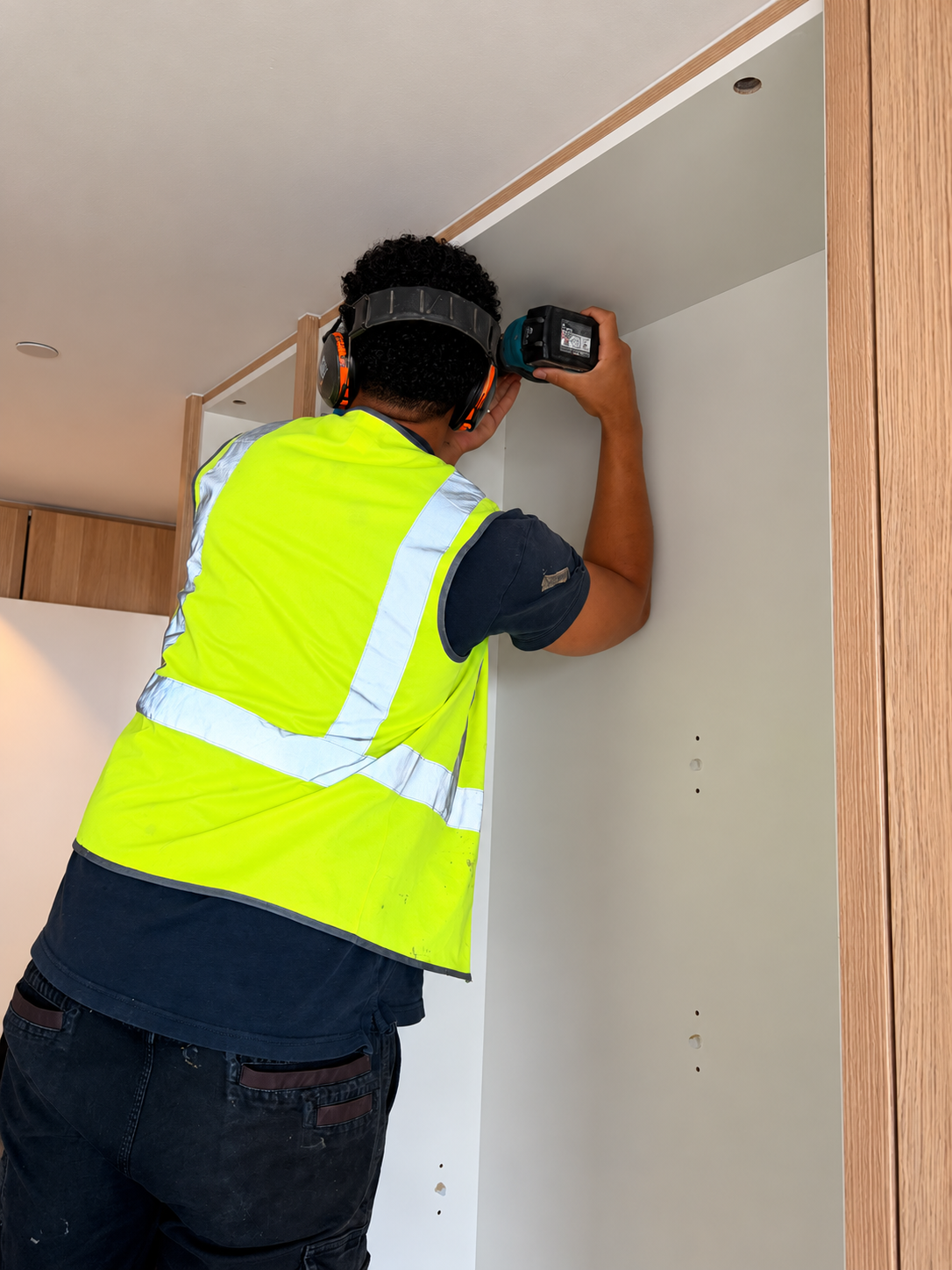 UPJ installer wearing hearing protection and a high-visibility vest while working on cabinetry